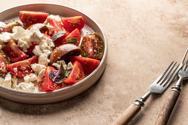 Tomatensalade met fetakaas en kruiden geserveerd met bestek op beige achtergrond met tekstruimte