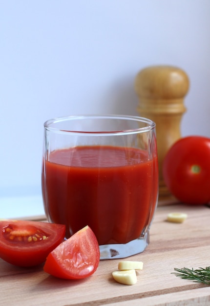 Tomatensap in een glas glas met tomaten knoflook zout op een houten plank