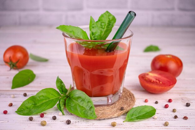 Tomatensap met kruiden in een glas op een witte houten achtergrond.