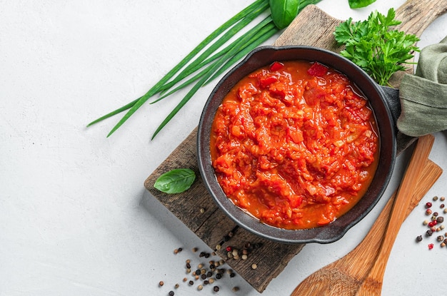 Tomatensaus in een koekenpan en verse kruiden op een grijze achtergrond