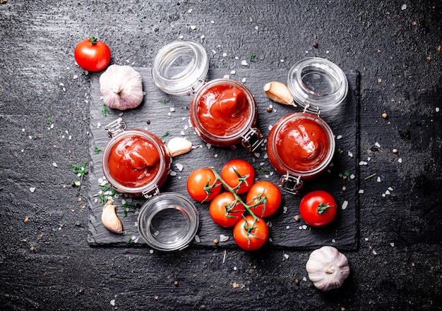 Tomatensaus in glazen potten op een stenen bord met kruiden