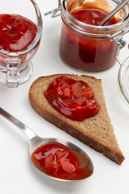 Tomatensaus in lepel en op stuk brood. Saus in pot en in kom. Detailopname. Witte achtergrond.