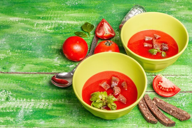 Tomatensoep met basilicum in kommen. Rijpe groenten, verse groenten, geurige kruiden. Houten tafel