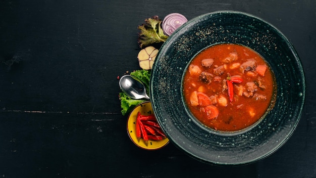 Tomatensoep met rundvlees en chilipepers in chervrniy plaat Op een houten tafel Bovenaanzicht Kopieer de ruimte