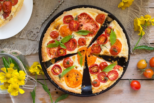 Tomatentaart gemaakt met kruimeldeeg, rode en gele tomaten, kaas en room. Concept het gezonde eten of vegetarisch voedsel op rustieke houten achtergrond