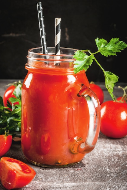 Tomatesap in metselaarkruik met tomaten en greens op een grijze concrete lijst.