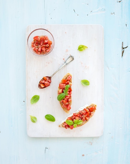 Tomato and basil bruschetta sandwich on white wooden serving board over rustic blue background top view