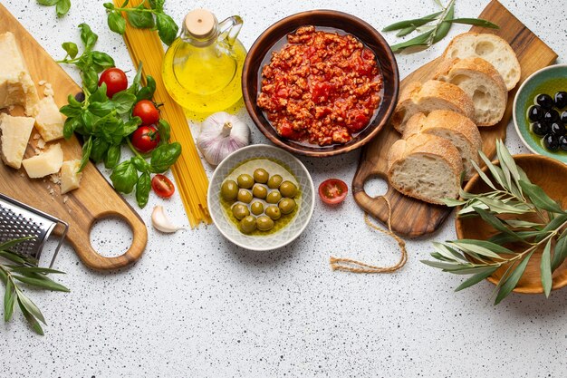 Tomato Bolognese sauce, spaghetti, cheese parmesan, olives, ciabatta, snacks on white rustic background. Ingredients for cooking Italian pasta or mediterranean healthy dinner, top view, copy space