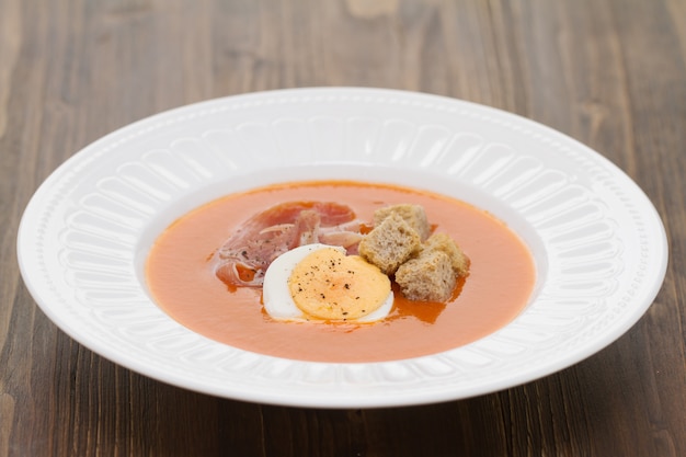 Томатный холодный суп с яйцом и хамоном на белом блюде