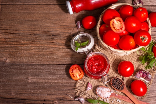 Tomato confiture, jam, chutney, sauce in a glass jar. Homemade preservation concept. Fresh tomatoes, spices, garlic, greens, sea salt. A modern hard light, dark shadow, vintage wooden table, top view