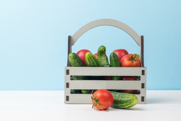 A tomato and a cucumber next to a full box on a white table.