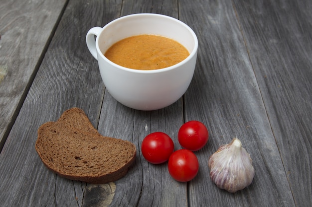 Tomato gazpacho soup with bread and garlic in white bowl on wooden