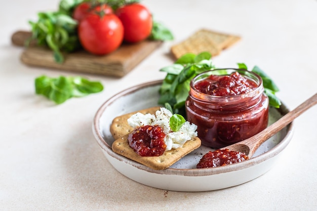 Tomato jam confiture or sauce in glass jar with crackers and green leaves salad Unusual savory jam