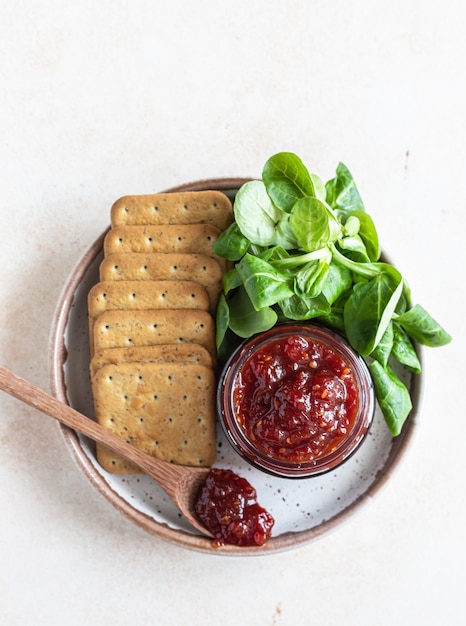 Tomato jam confiture or sauce in jar with crackers Unusual savory jam Mediterranean cuisine