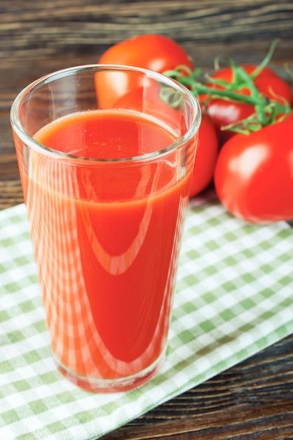 Tomato juice in glass and fresh tomatoes on wooden table