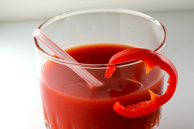 Tomato juice in a glass with a cocktail tube and a slice of sweet pepper close-up