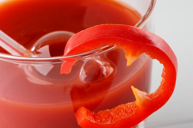 Tomato juice in a glass with a cocktail tube and a slice of sweet pepper close-up