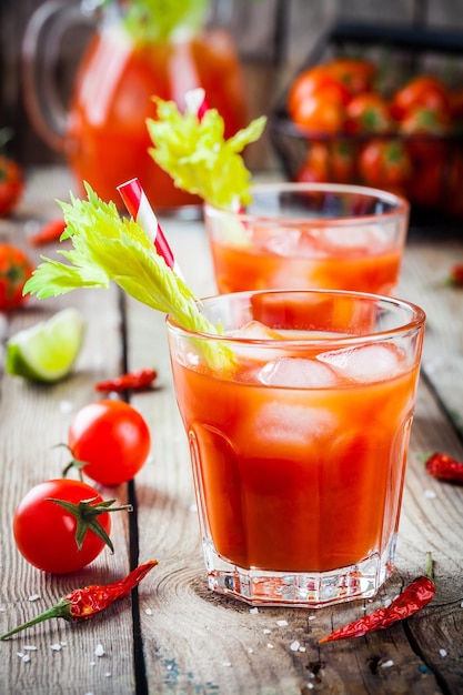 Tomato juice with celery and ice in glasses on a wooden table