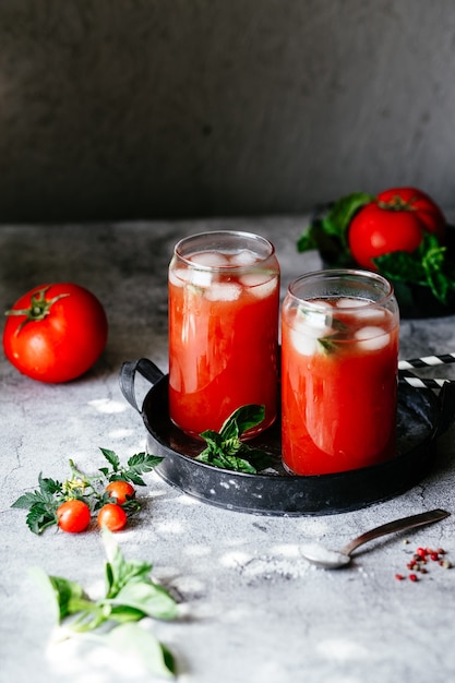 Tomato juice with ice in a glass on a gray background