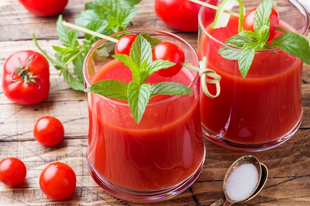 Tomato juice with mint in glass and fresh tomatoes on a wooden table. Healthy organic food concept.