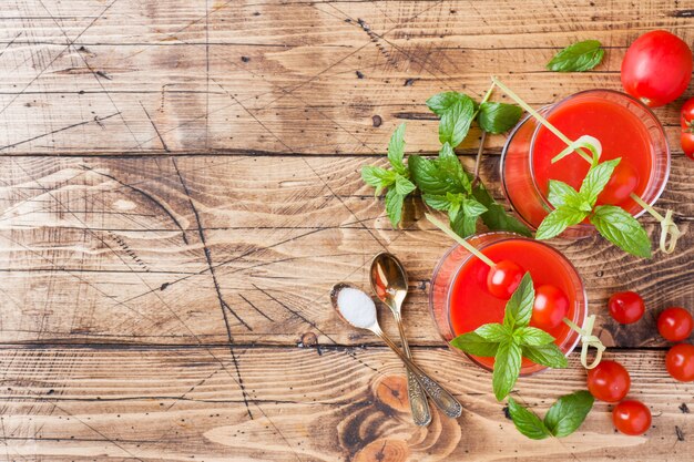 Tomato juice with mint in glass and fresh tomatoes on a wooden table. Healthy organic food concept.