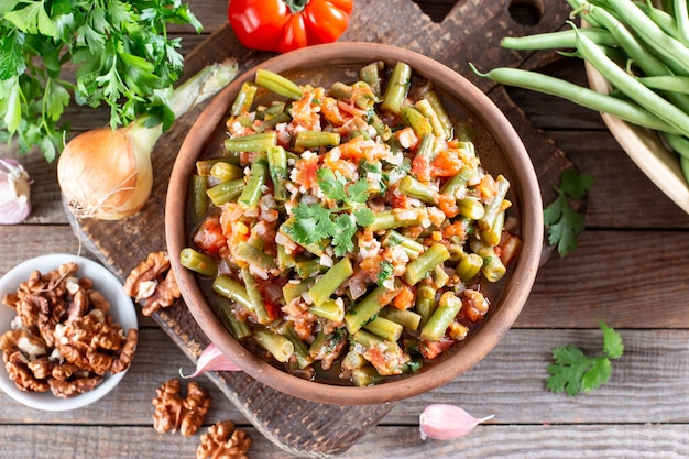 Tomato lobio of green bean pods in a bowl on a wooden background. Lenten dish. Flat lay, top view. Close-up