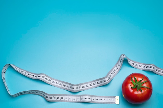 Tomato and measuring tape on the blue background. The concept of diet. Free space for text. Top view, flat lay. Overeating control, diet, nutritionist.