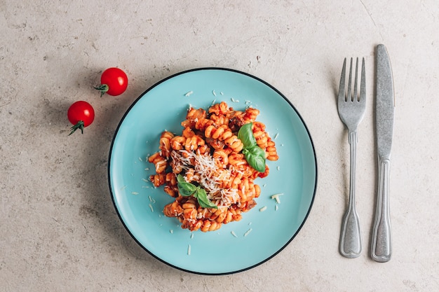 Tomato pasta with cheese and basil on a blue plate over a stone background minimal flat lay