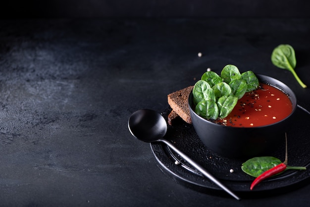Tomato puree soup with spinach in a black bowl, close-up