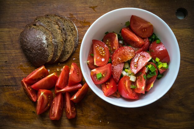 Insalata di pomodori con olio d'oliva e aceto balsamico in una ciotola su sfondo di legno