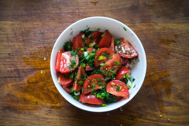 Tomato salad with olive oil and balsamic vinegar in bowl over wooden background