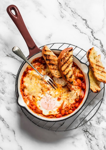 Tomato sauce beans cheese eggs baked shakshuka in a ceramic frying pan with a grill crispy bread on a light background top view