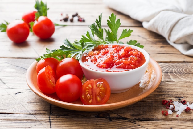 Pasta della salsa al pomodoro in una ciotola e pomodori freschi con prezzemolo su una tavola di legno copi lo spazio