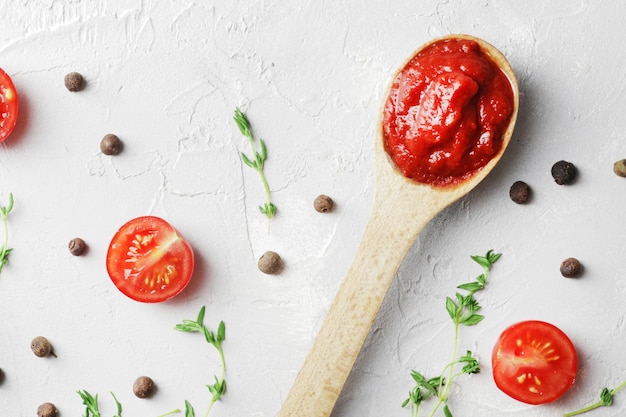 Tomato sauce in a wooden spoon and spices on a marble background