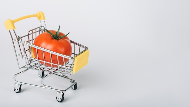 Foto pomodoro nel carrello della spesa su superficie bianca