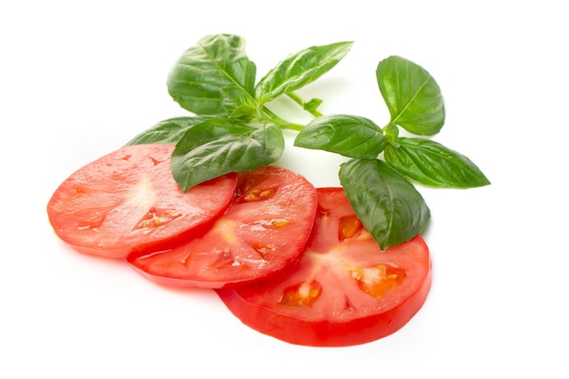 Tomato slices with basil leaves on a white background.