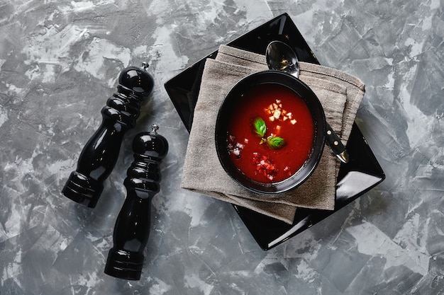 Tomato soup in a black bowl on a gray stone background. View from above. Copy space. Gray background. calm light. Food concept