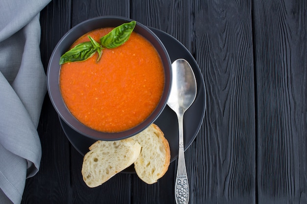 Zuppa di pomodoro nella ciotola scura su fondo di legno nero.vista dall'alto.spazio copia.