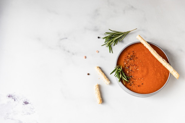 Tomato soup garnish with ground pepper rosemary and bread sticks light background