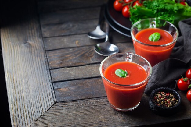 Tomato soup in a glass bowl on dark wooden table over balck