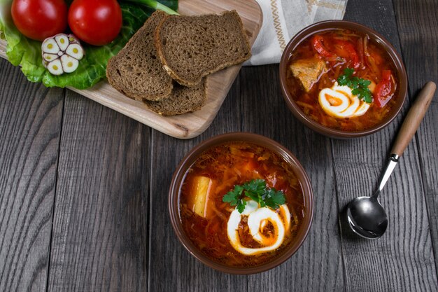 Tomato soup . Traditional  Ukrainian beetroot and tomato soup - borsch in clay pot with sour cream, garlic, herbs and bread on dark wooden table.Ingredients on table