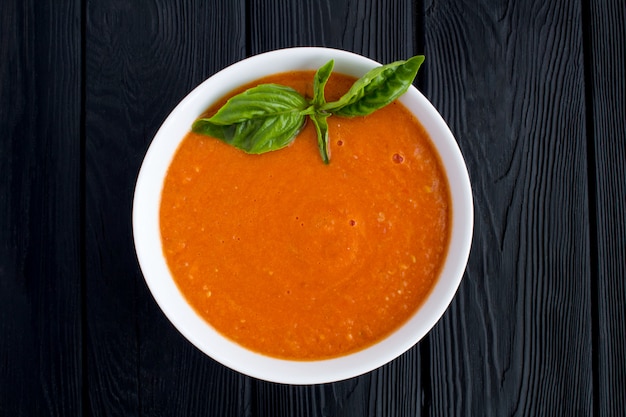 Tomato soup in the white bowl on the black wooden background