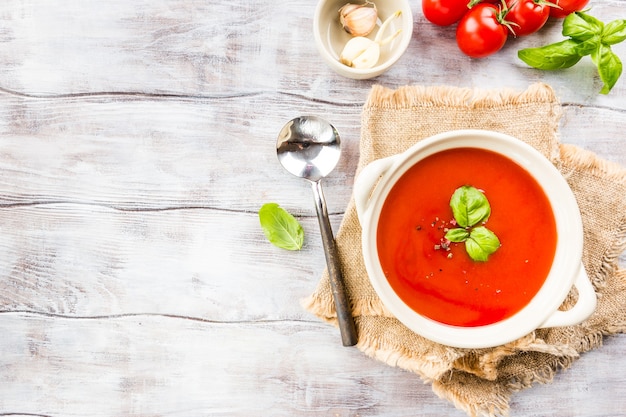 Tomato soup in a white bowl on wooden table, top view