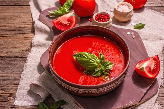 Tomato soup with basil in a bowl. Ripe vegetables, fresh greens, fragrant spices. Vintage wooden table, close up