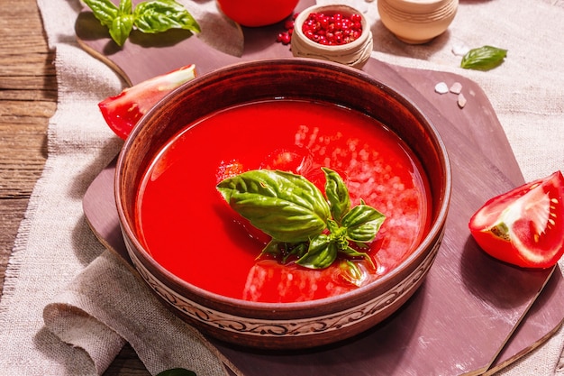 Tomato soup with basil in a bowl. Ripe vegetables, fresh greens, fragrant spices. Vintage wooden table, close up