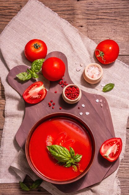 Tomato soup with basil in a bowl. Ripe vegetables, fresh greens, fragrant spices. Vintage wooden table, top view