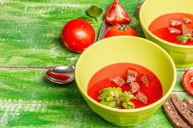 Томатный суп с базиликом в мисках. Спелые овощи, свежая зелень, ароматные специи. Деревянный стол