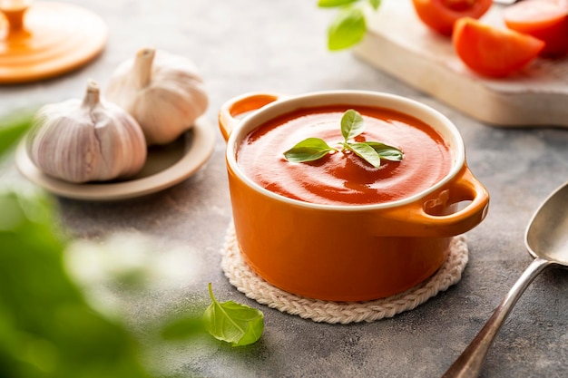 Tomato soup with fresh basil in orange bowl Bright background Healthy food concept