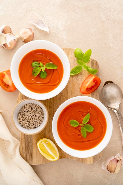 Tomato soup with fresh basil in white bowls Served with sunflower seeds Bright background Top view copy space