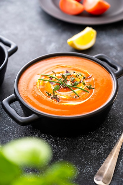 Tomato soup with fresh herbs in black bowl Dark background Vegan creamy soup